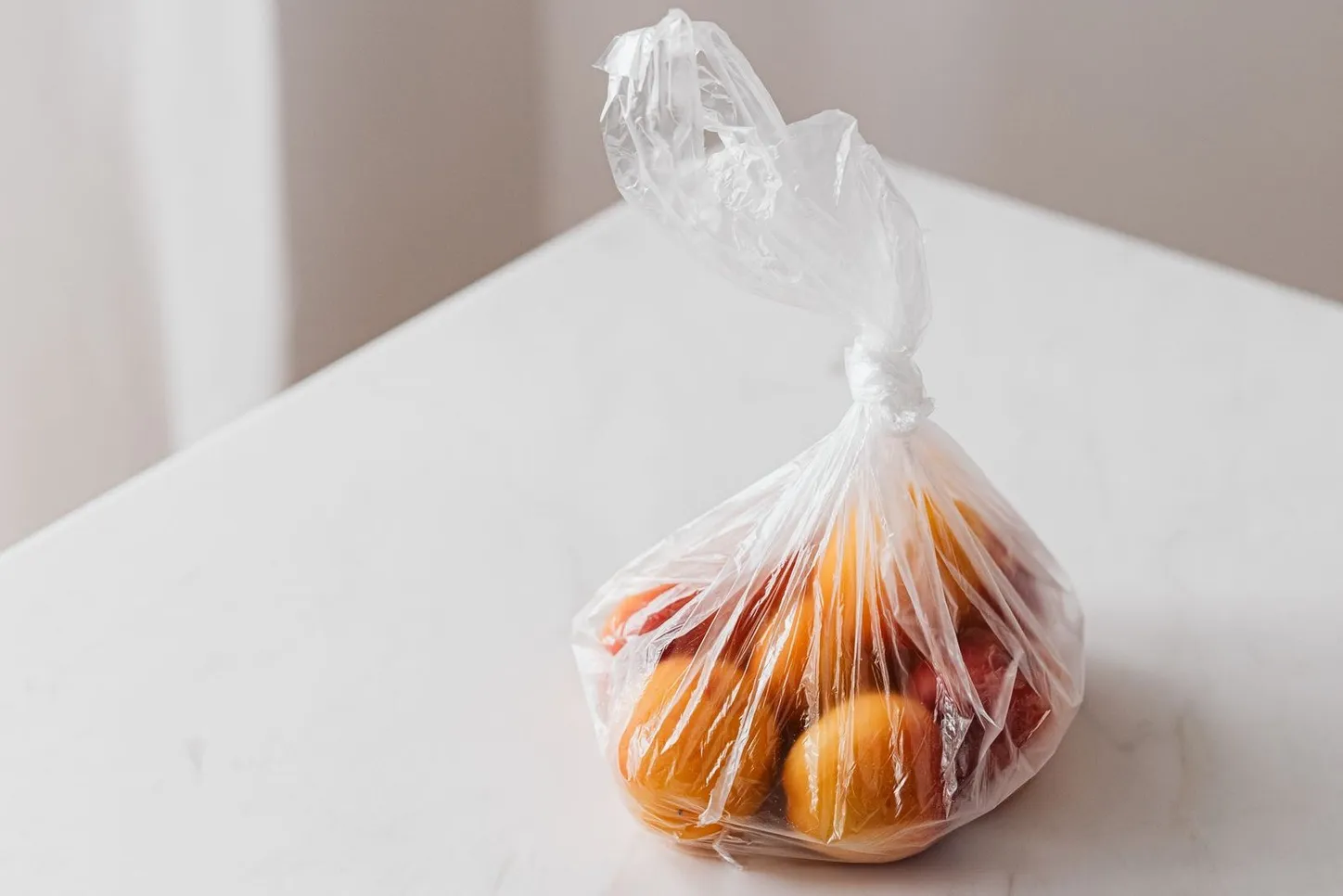 Fruit packed in a knotted clear LDPE grocery bag on a white table